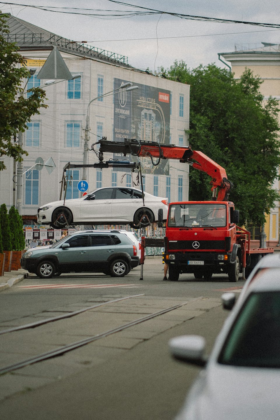 Czerwona laweta podnosi biały sedan na ulicy miasta.